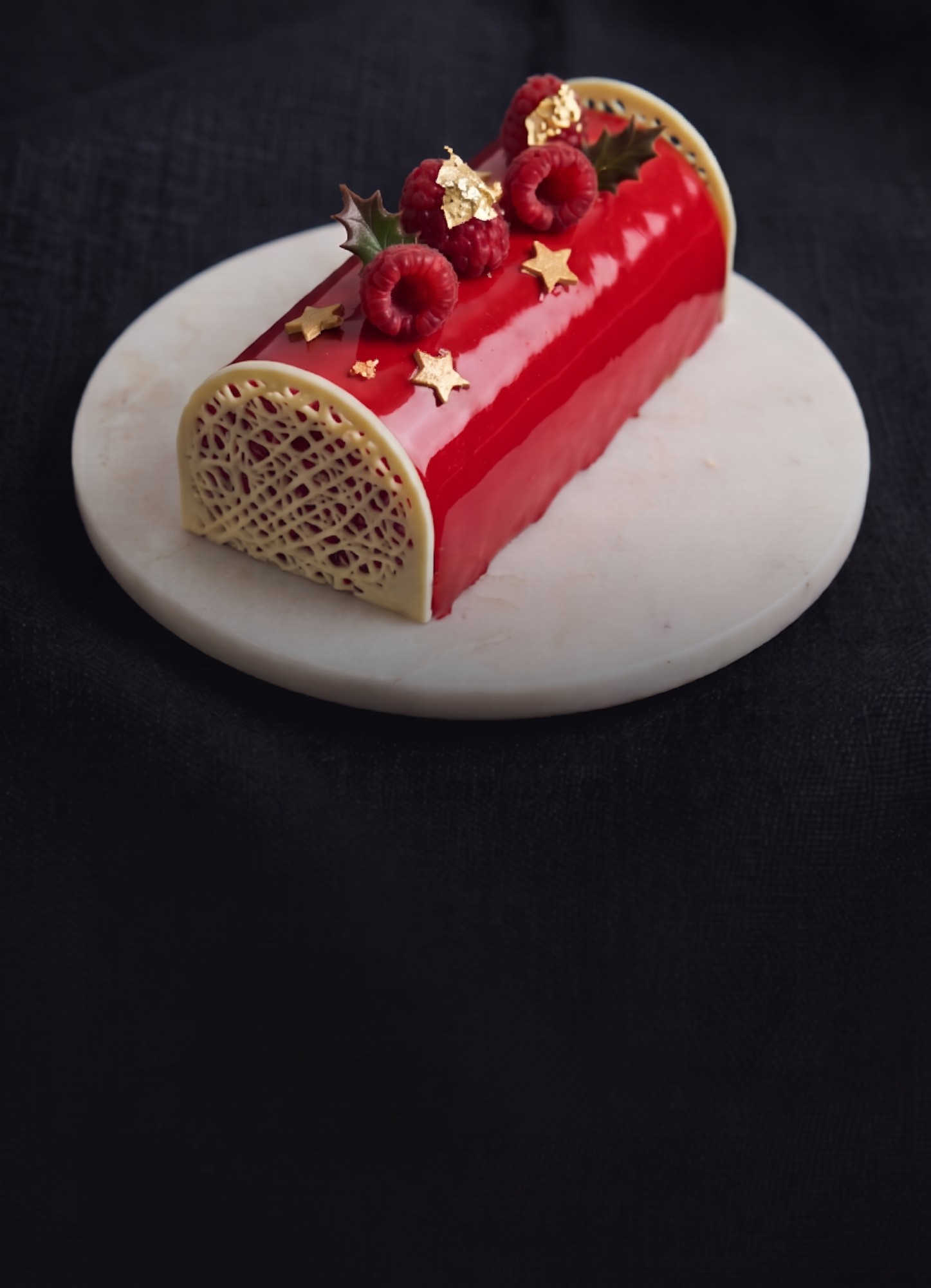 Bûche de Noël maison au glaçage rouge, framboises et dentelle de chocolat blanc